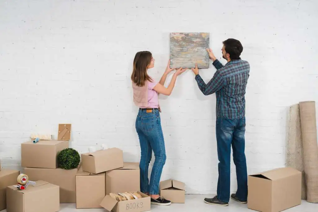 How to Pack Paintings for Moving: The Complete Guide-2 rear-view-young-couple-placing-picture-frame-white-wall-with-cardboard-boxes_23-2148095447